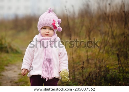 Happy baby girl in a pink hat and scarf laughs in autumn