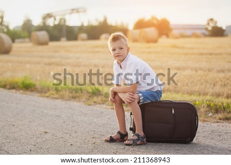 the child sits on a suitcase in the summer sunny day, the traveler