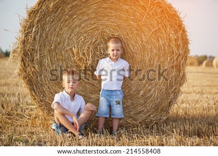 Two little brothers sitting near a haystack in wheat field on warm and sunny day