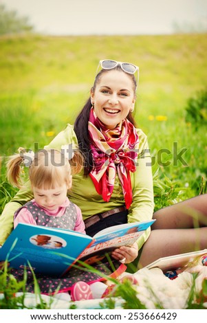 Mother with daughter read a book in the park in the warm spring day