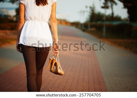 Picture of young woman hand with shoes in the park. Rear view