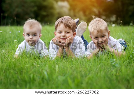 Three happy children (brothers)  resting on the green grass