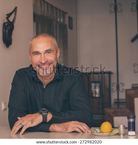 Happy mature man  enjoying drinking tequila  in  kitchen of own house, toned image