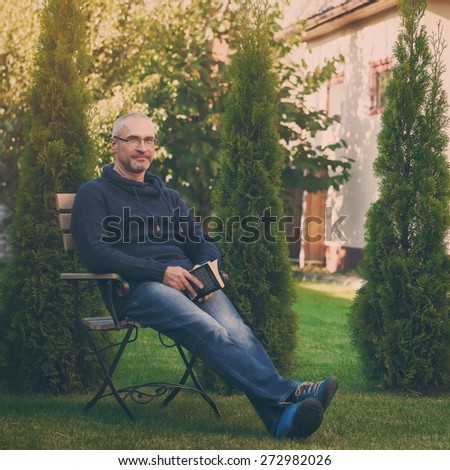 The mature senior man reading novel in country home garden, toned image