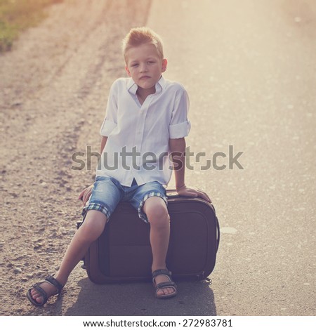 the child sits on a suitcase in the summer sunny day, the traveler,toning image