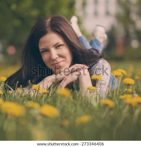 pretty woman lying down on dandelions field, happy cheerful girl resting on dandelions meadow.Toned image