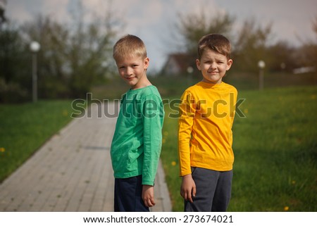 Two children standing back to back. Two cheerful boys of the friend. Outside