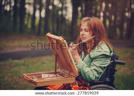 Portrait young woman sitting in a wheelchair , smiling and painting on small easel. Toned image