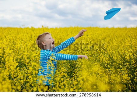 Happy boy started the blue paper aiplane in the sky over the yellow blossoming field in a sunny day