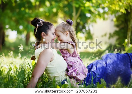Happy family. Mother and the daughter look at each other, smile, embrace, sit on a grass in the sunny summer day