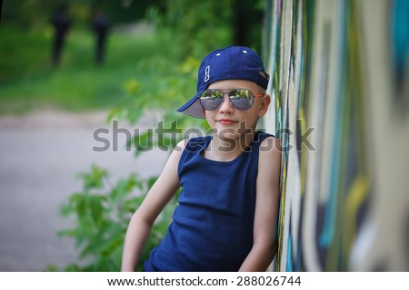 Portrait of Fashionable little boy in sunglasses and cap.Graffiti background.  Summertime. Outdoors