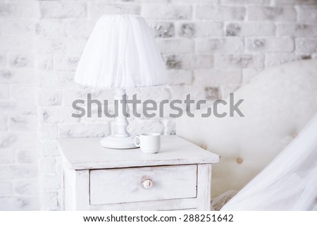 Interior. White lamp and  cup of coffee on a bedside table in a bedroom in early  morning.