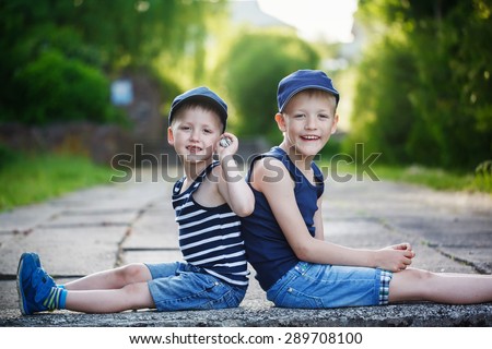 Two adorable little brothers sitting on stone on warm and sunny summer day. Sitting back to back, looking at the camera