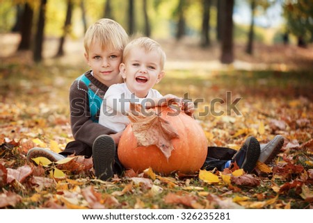 Two little brothers sitting on grass and embracing with huge pumpkin in autumn day