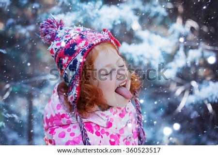 Portrait of a cute little girl who catches snowflakes mouth in winter day.