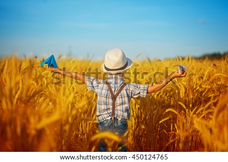 Cute child walking in the wheat golden field on a sunny summer day. 
Boy starts paper plane. Nature in the country.Back view