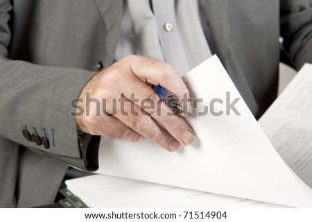 Businessman going through contract pages before to sign it. Focus on hand with a pen and pages.