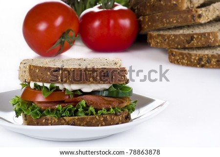 Freshly made bacon sandwich with sliced bread and tomatoes on the background