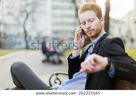 Businessman looking at his wrist watch on a sunny day in a city park
