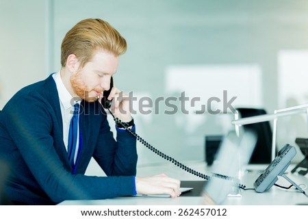 A handsome male, red haired worker in a call center office talking on a phone