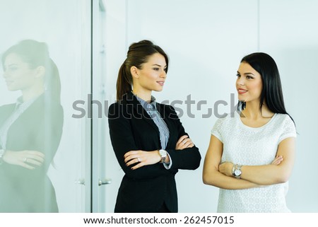 Two businesswomen talking in an office with reflection showing on the glass wall next to them
