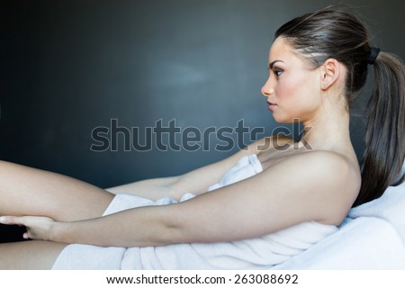 Beautiful, young lady lying on a massage table photographed from the side while holding her leg