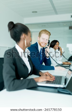 A beautiful, black, young woman working at a call center in an office with her red haired colleague talking to a customer