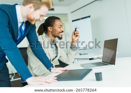 A black young man with dreadlocks and a young handsome red haired businessman discussing graphics design flaws in a nice white office