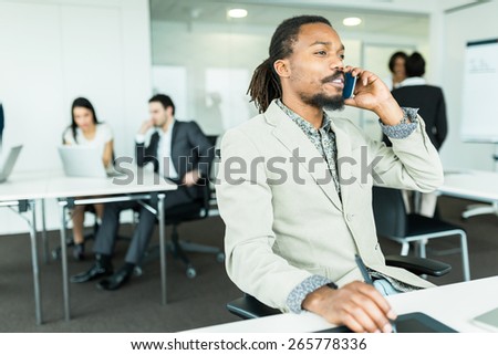 Black handsome graphics designer  with dreadlocks using digitizer in a well lit, tidy office environment and talking on the phone while his colleagues are working overtime in the background
