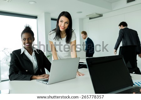 Black and white businesswomen looking at a laptop and working in a neat office environment
