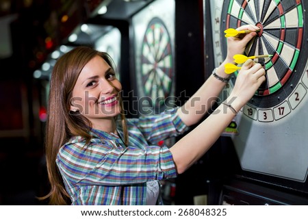 Young beautiful woman playing darts in a club and smiling