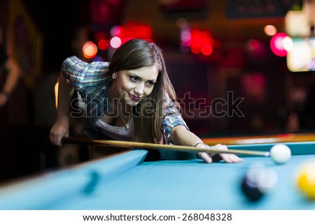 Young beautiful young lady aiming to take the snooker shot while leaning over the table in a club