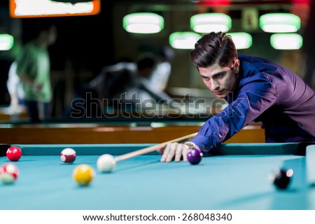 Young handsome man leaning over the table while playing snooker