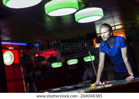 Handsome young snooker player bending over the table in a bar with beautiful ambient lighting