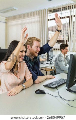 Beautiful young woman and a man raising hands in classroom in  while sitting in front of a desktop