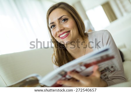 Beautiful woman on a sofa reading a paper in a well lit stylish  living room
