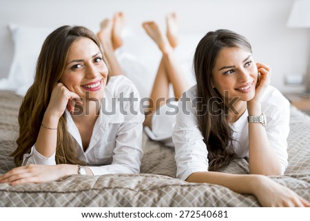 Two beautiful girls talking and smiling while lying on a luxurious  bed