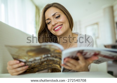 Beautiful woman on a sofa reading a paper in a well lit stylish  living room