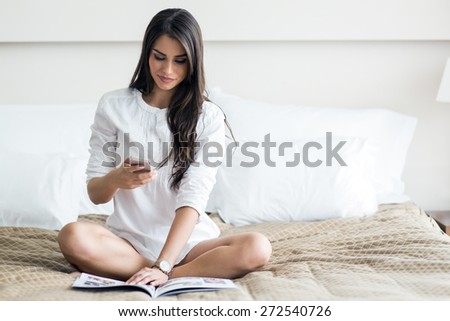 Beautiful woman in a shirt talking on the phone and reading the morning paper on the luxurious bedroom bed