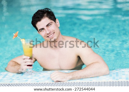 Handsome young man drinking a cocktail while relaxing in a swimming pool