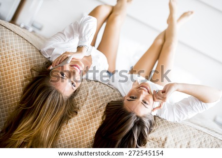 Two stunning women talking on phones with their hair falling off the bed as they lie upside down