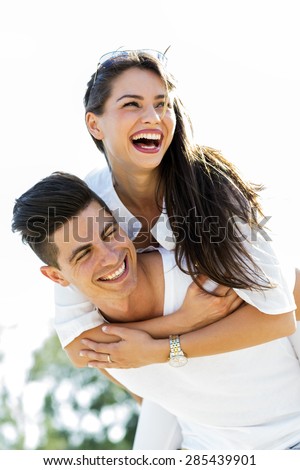 Cheerful handsome man carrying his girlfriend on his back on the beach