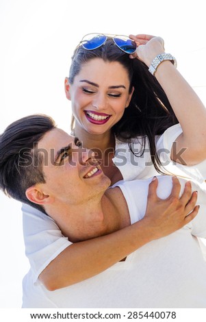 Cheerful handsome man carrying his girlfriend on his back on the beach