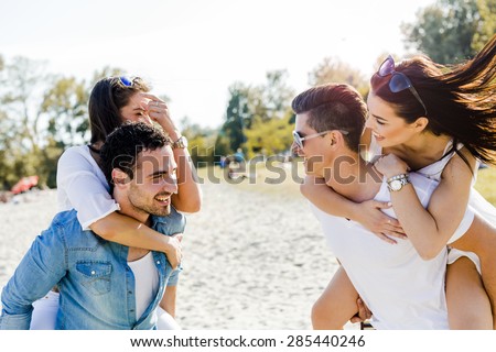 Group of young happy people carrying women on a sandy beach piggyback