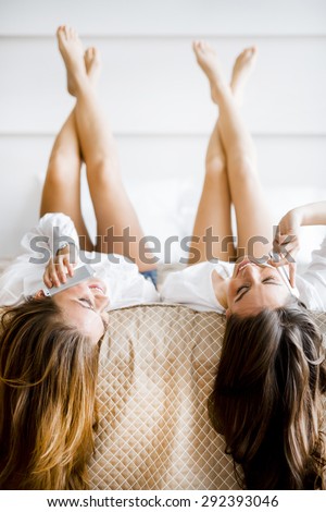 Two stunning women talking on phones with their hair falling off the bed as they lie upside down