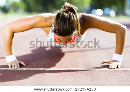 Focused young beautiful woman doing push-ups outdoors on a hot summer day