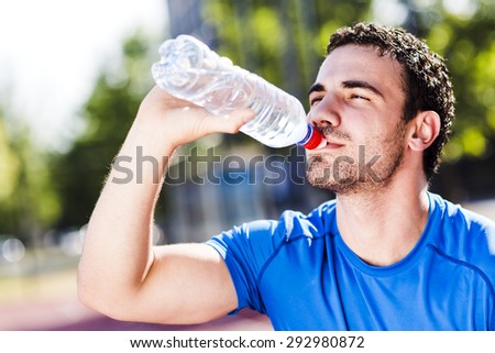 Young handsome athletic man drinking water during a hot summer day to refresh his body and soul
