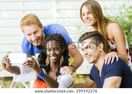 A group of friends sitting a table and talking smiling  while taking selfies on a hot summer day