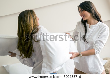 Two beautiful girls fighting with pillows in a luxurious bedroom