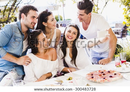 Group of young beautiful people sitting in a restaurant and taking a selfie while smiling